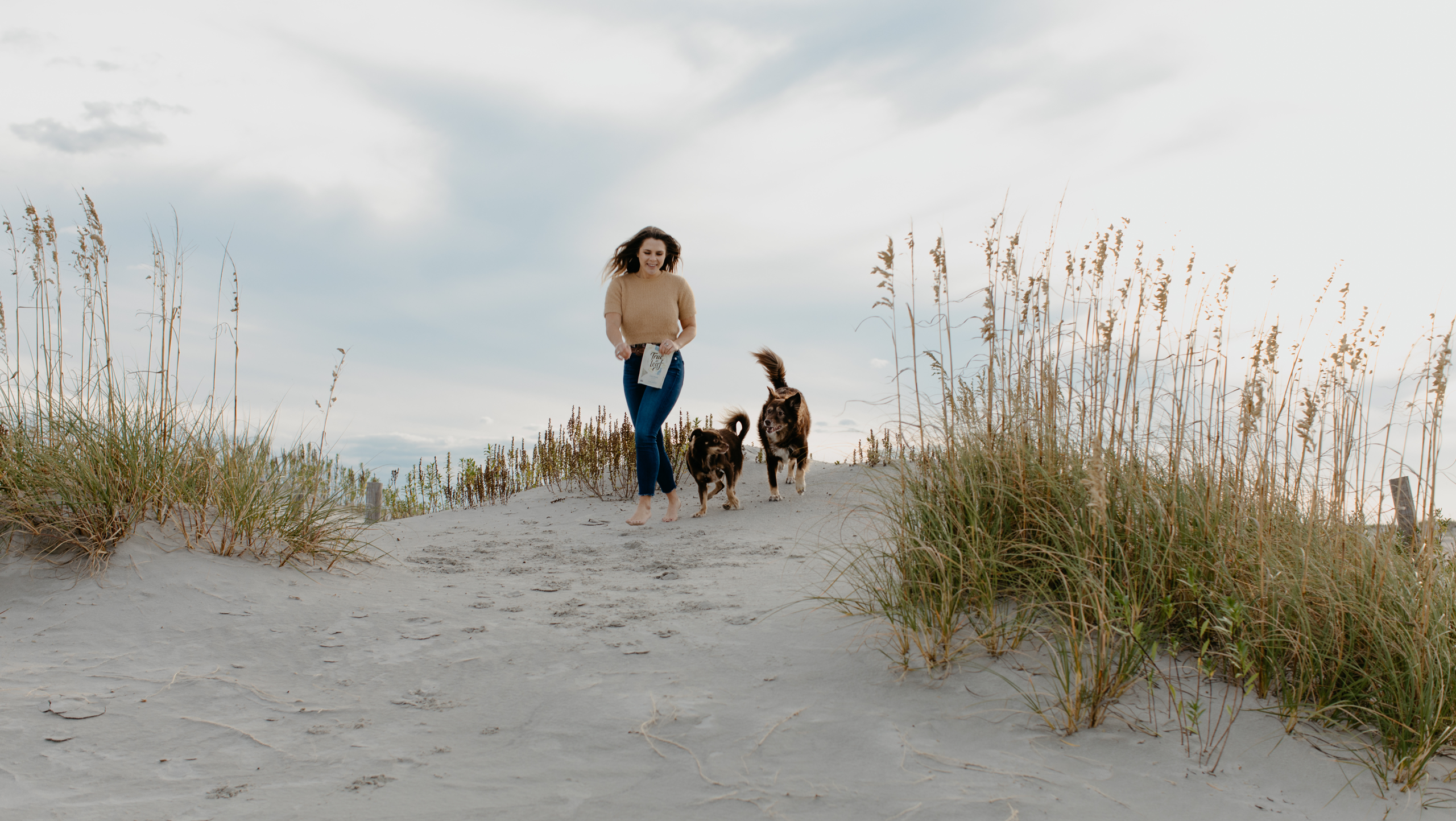 Woman walking on the beach with two dogs and True Leaf products.